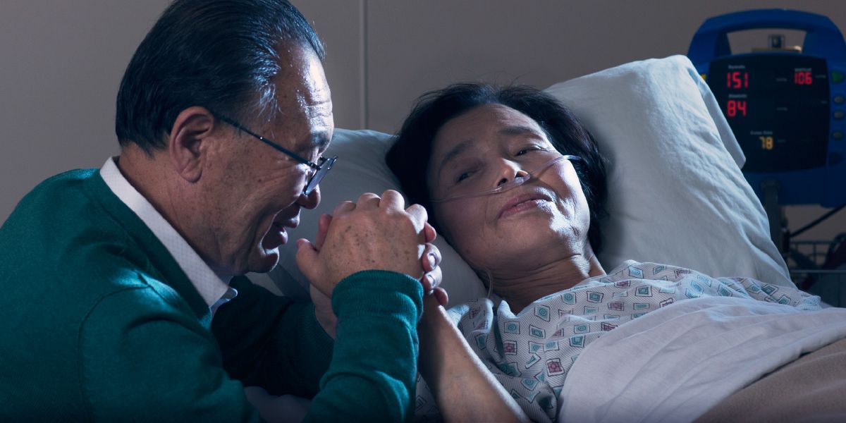 Una cristiana está en una cama de hospital. Su esposo sostiene su mano y ora con ella