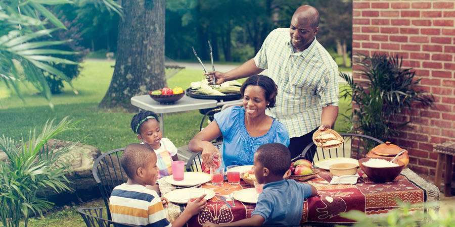 Una familia disfruta de una comida en el patio de la casa. El padre cocina y lleva la comida a la mesa.