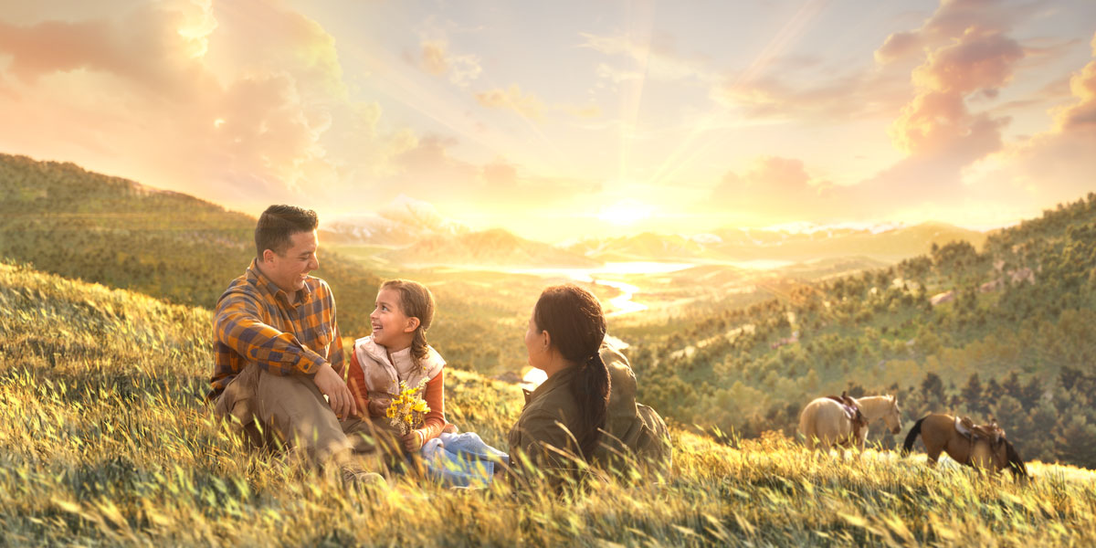 أفراد عائلة يضحكون معًا وهم جالسون على تلة في فردوس على الأرض.‏ بالقرب منهم هناك حصانان يرعيان
