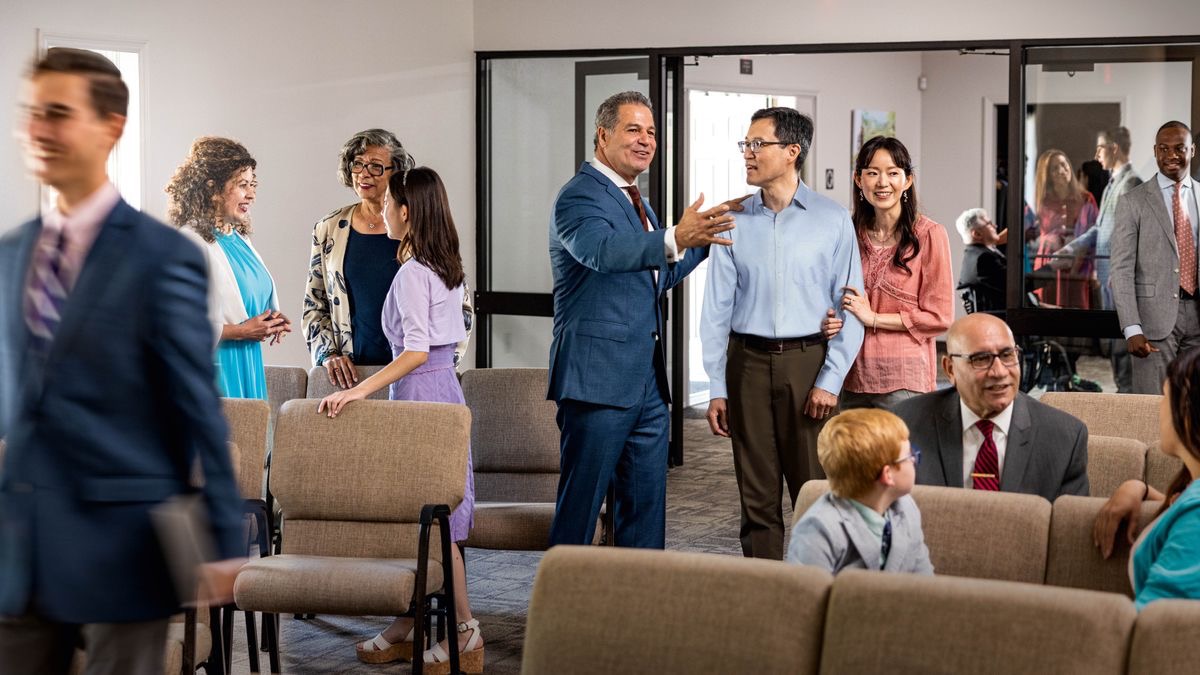 Des frères et des sœurs d’âges et d’origines différents discutent joyeusement entre eux avant une réunion de l’assemblée. Un frère accueille un couple qui n’est pas Témoin.