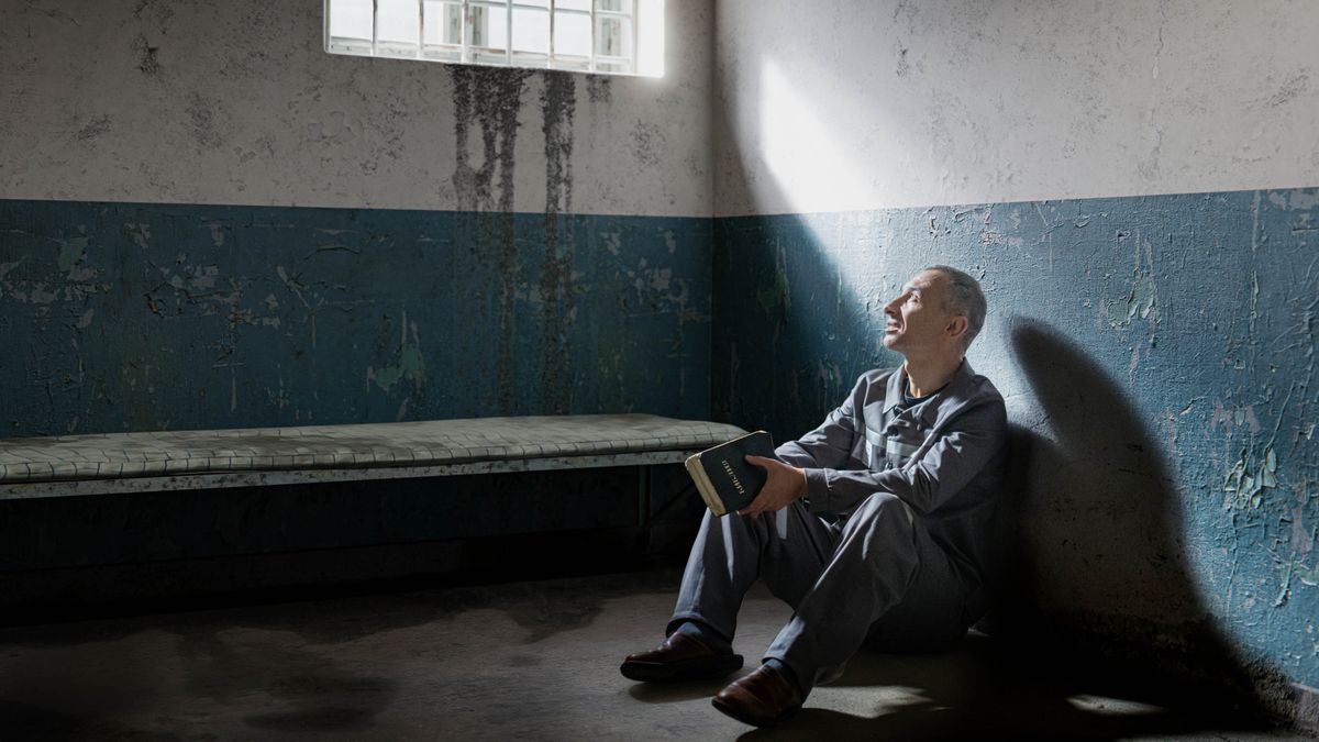 Dans une cellule de prison, un frère tient dans ses mains une bible et regarde par la fenêtre.