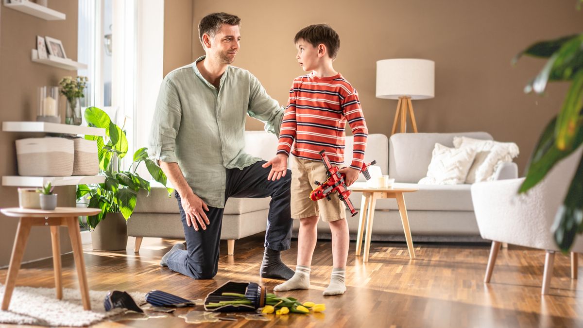 Un père écoute patiemment son jeune fils lui expliquer qu’il a involontairement cassé un vase contenant des fleurs en jouant avec son avion.