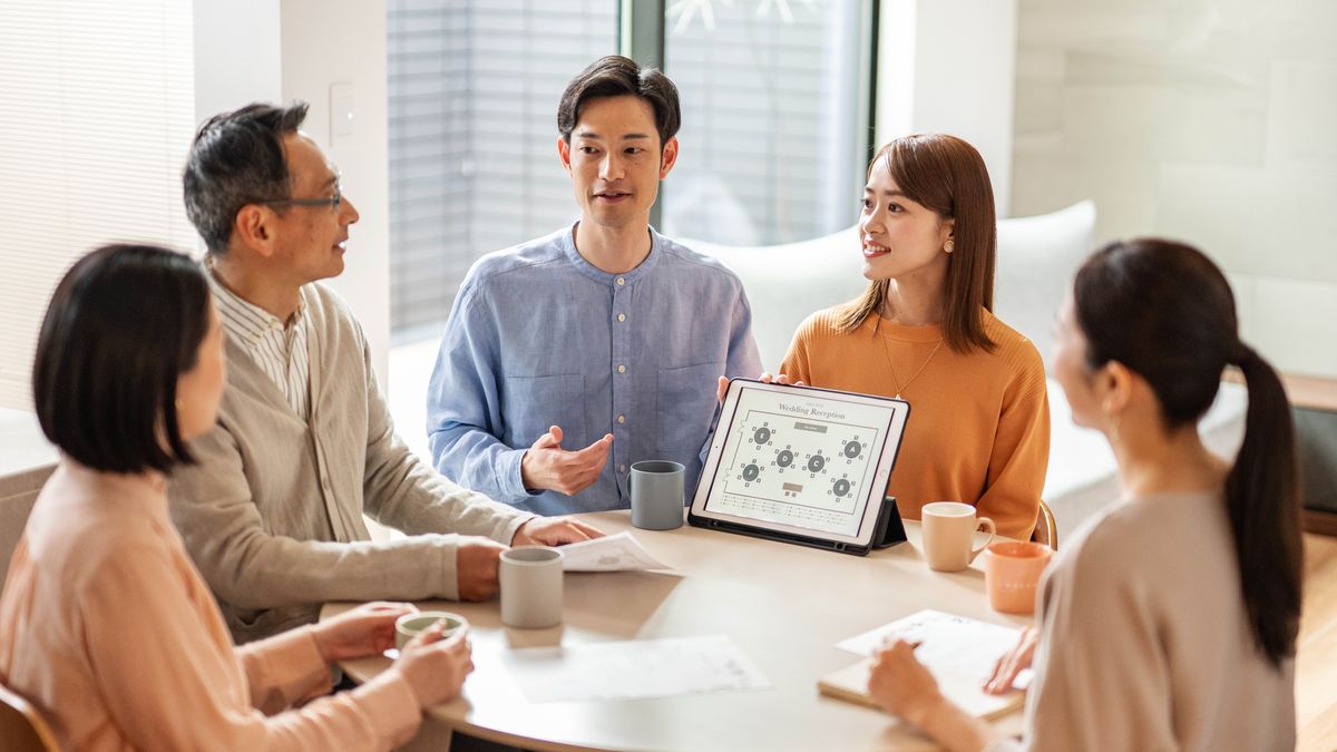 Un frère et une sœur qui sont fiancés discutent de l’organisation de leur mariage avec des amis qui les aideront. Le frère montre sur une tablette le plan de table du repas de mariage.