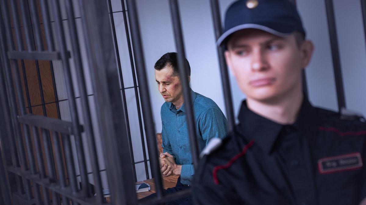 Dans une cellule de prison, un frère qui a des hématomes sur le visage prie tandis qu’un gardien se tient à proximité.