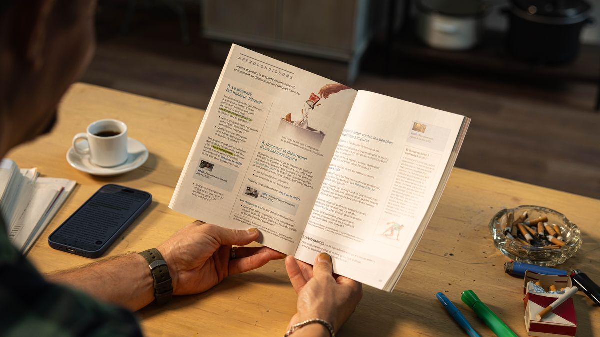 Un homme lit la leçon 40 du livre « Vivez pour toujours ! ». Sur son bureau, il y a un paquet de cigarettes et un cendrier rempli de mégots.