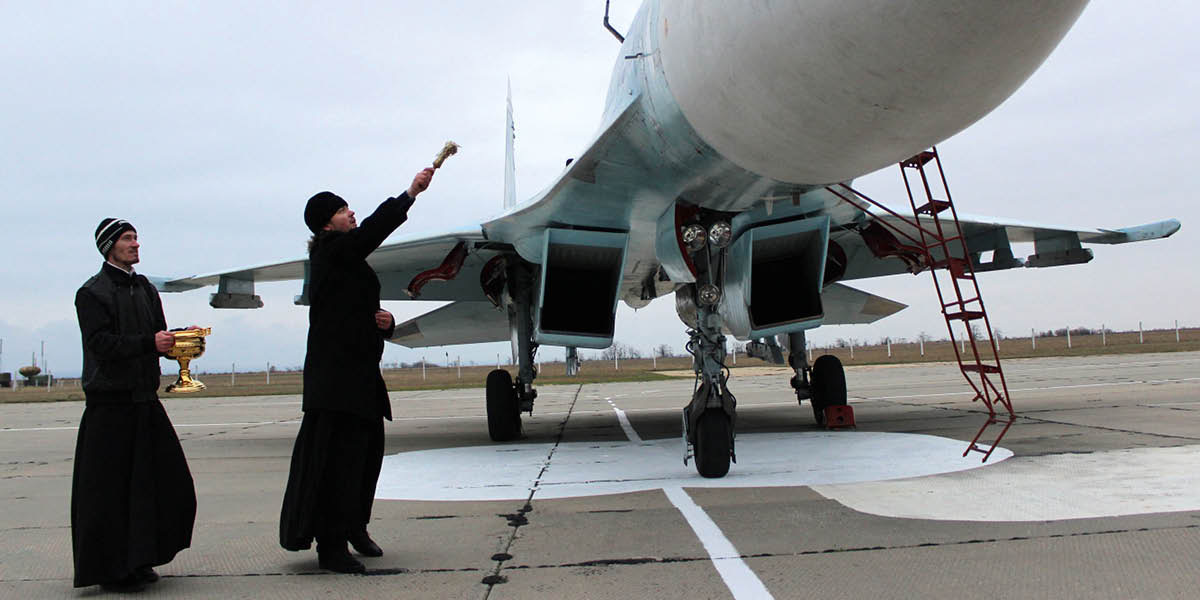 Свещеник поръсва боен самолет със светена вода и го благославя.