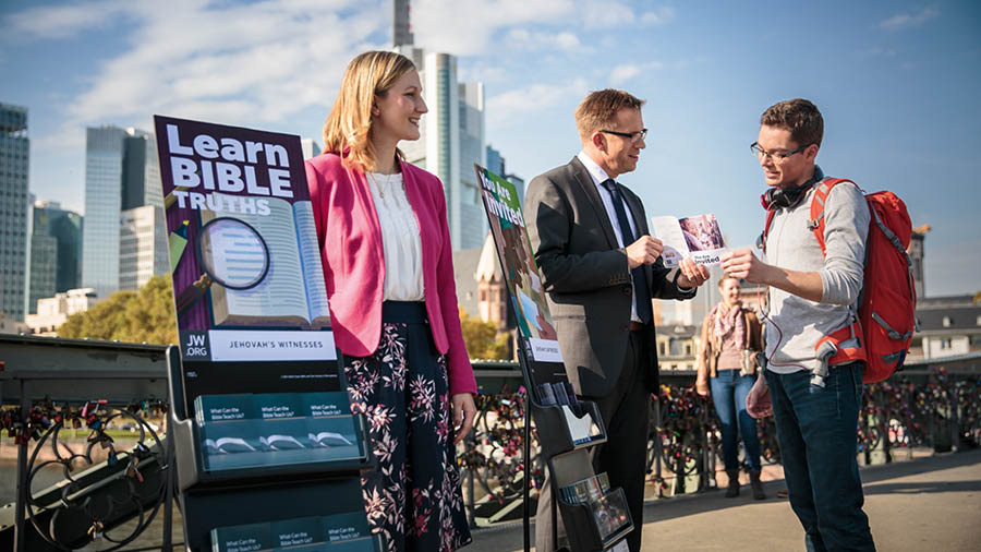 Свидетели на Йехова до колички с литература говорят с млад мъж.