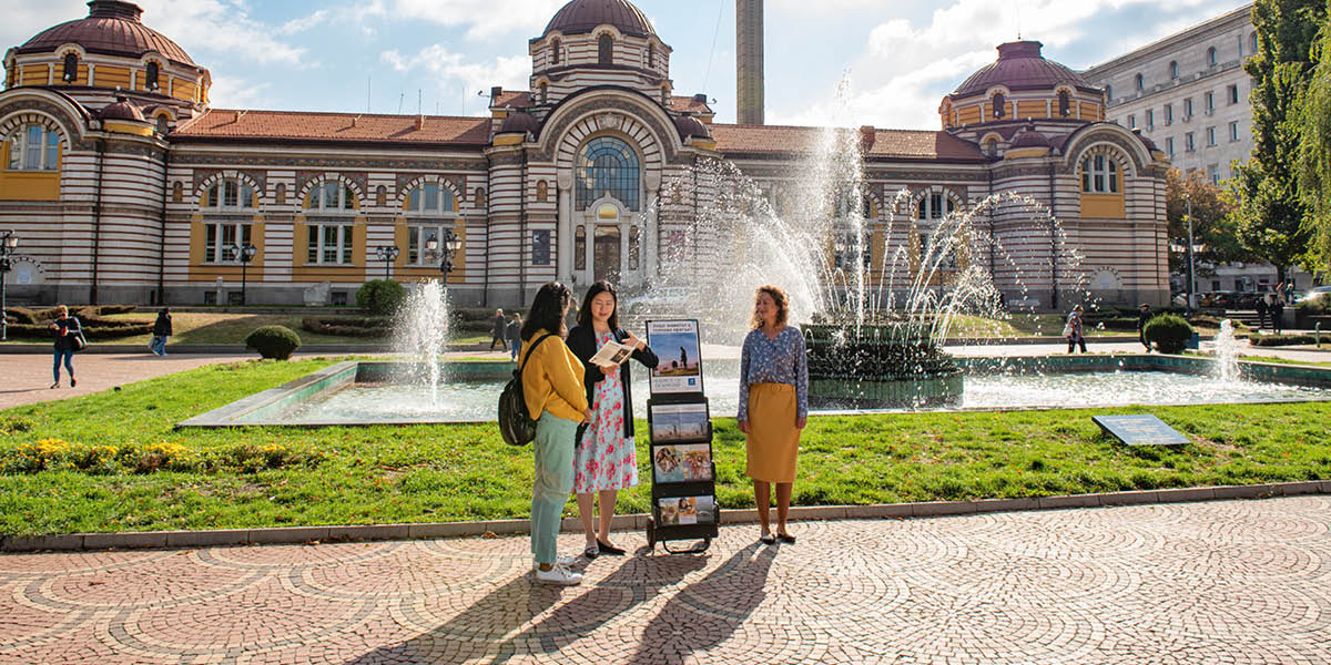 Dvě sestry stojí u stojanu s publikacemi a mluví s ženou o Bibli