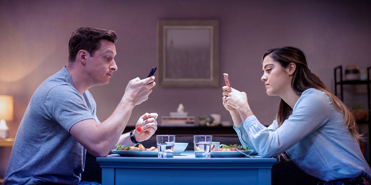 Manželé spolu večeří a přitom si každý něco prohlíží na svém telefonu.