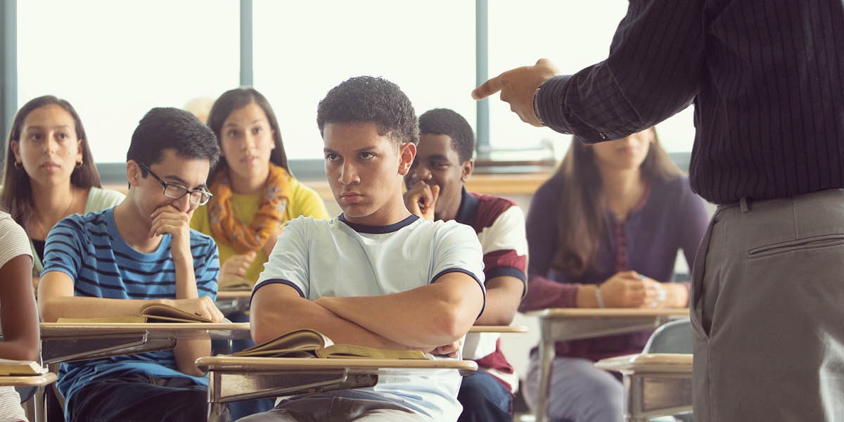 Student sedí ve třídě a učitel ho napomíná