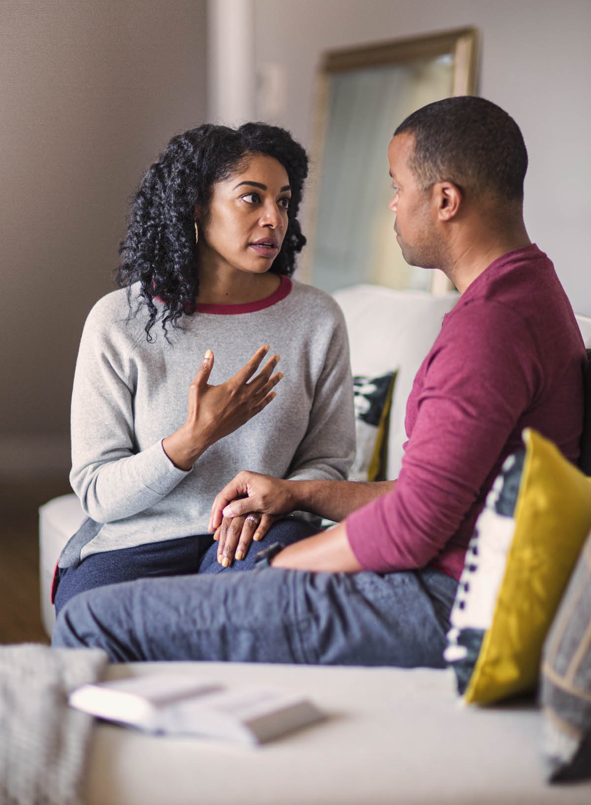 Un matrimonio conversando, tomados de la mano y sentados uno junto al otro. Hay una Biblia abierta junto a ellos