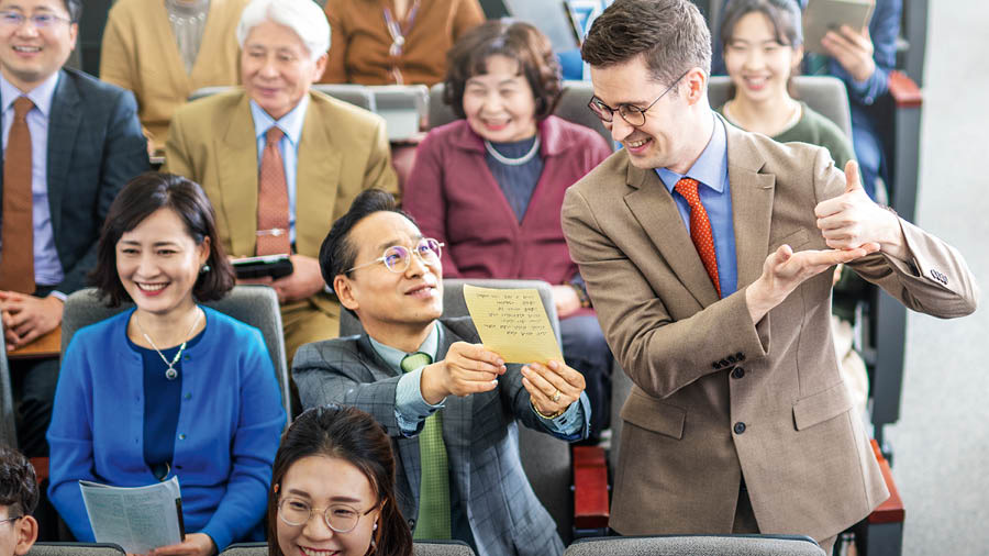 Durante una reunión, un hermano que está aprendiendo un idioma lee un comentario que ha preparado. Los demás lo miran con respeto.
