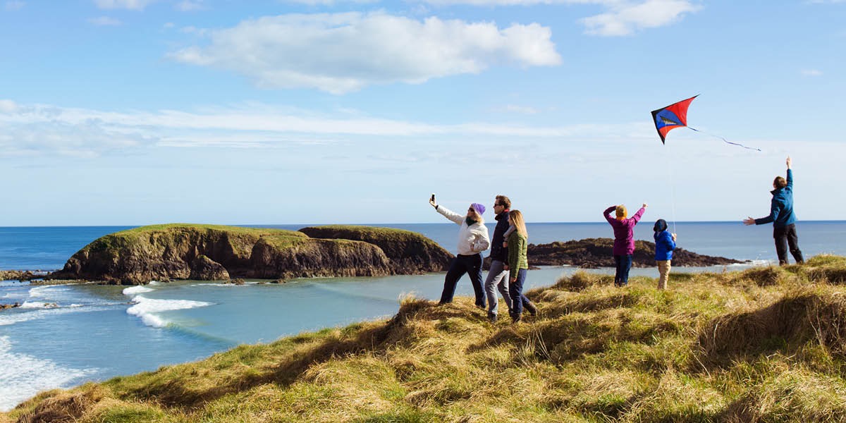Folk ved havet flyver med drage og tager billeder