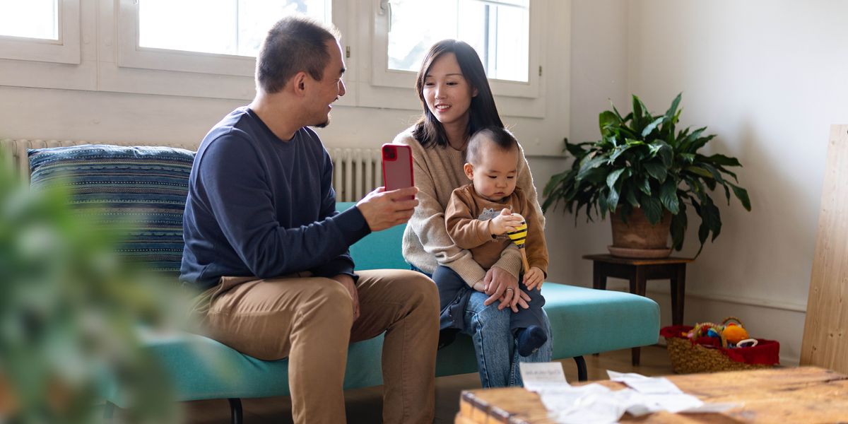 En mand viser sin kone noget på sin telefon mens hun sidder med deres lille søn.