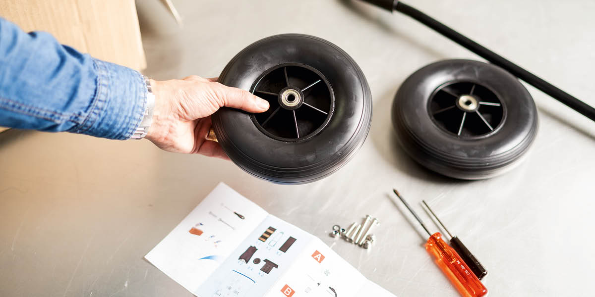 Brugsanvisning, værktøj og reservedele til en litteraturvogn, deriblandt hjul, en stang, skruer og møtrikker.