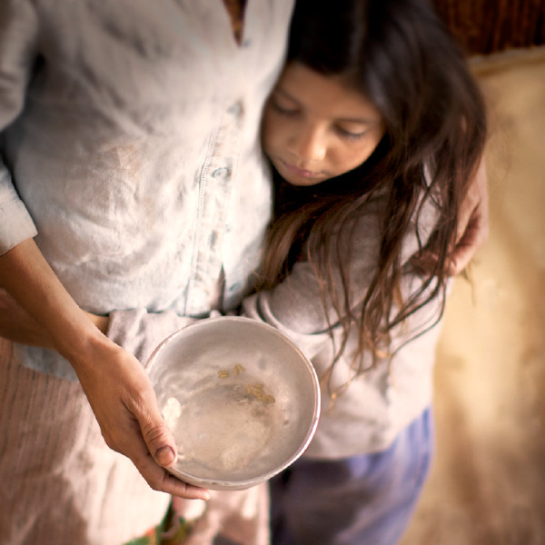 En kvinde står med en tom skål i hånden og holder om en lille pige