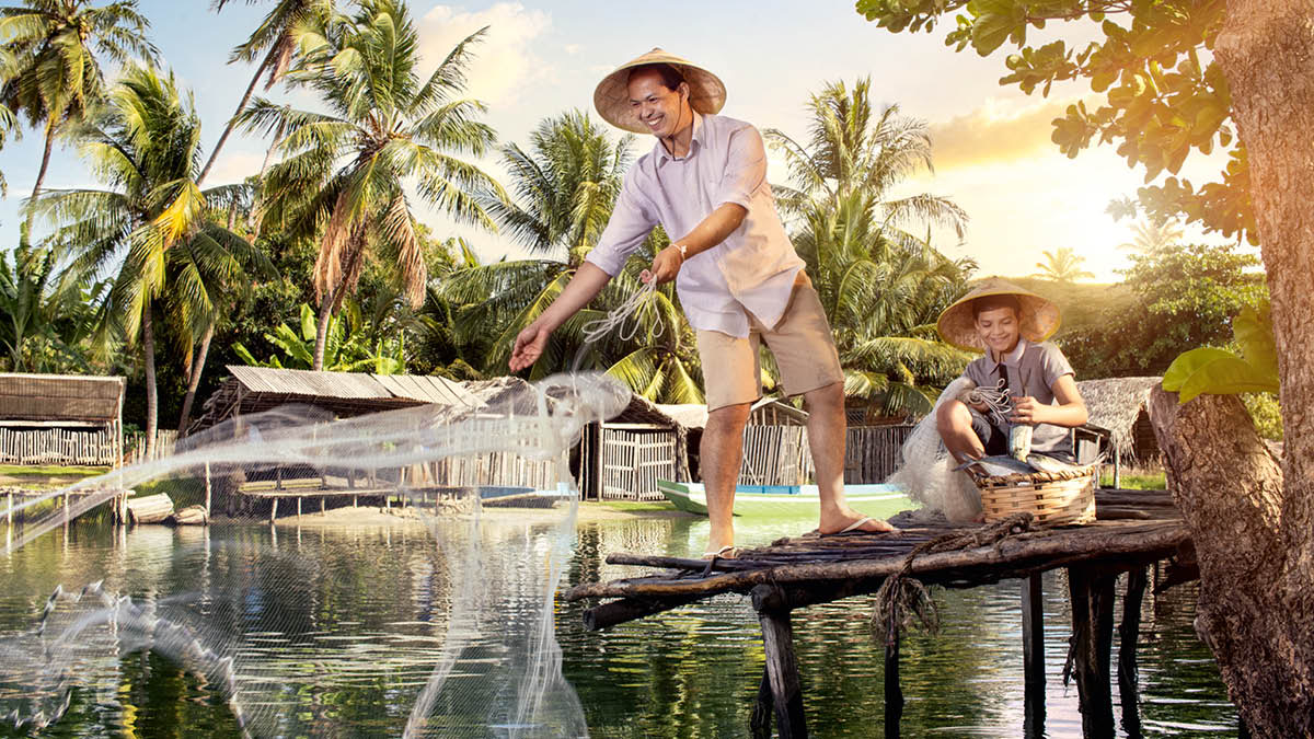 En bror står på en lille bro sammen med sin søn og kaster et fiskenet ud.