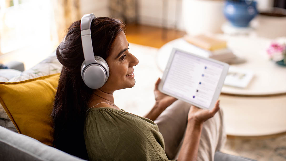 En søster sidder med høretelefoner på og lytter til en lydindspilning på sin tablet.
