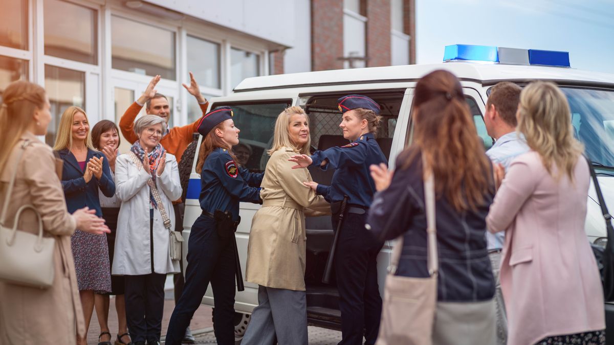 En søster bliver ført hen til en politibil af to kvindelige betjente. En gruppe af hendes trosfæller står og klapper af hende.
