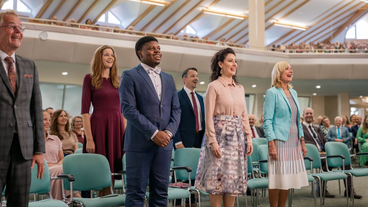 Ved de forreste rækker i en stævnehal har de der skal døbes, rejst sig op for offentligt at give udtryk for deres tro. Der er både mænd og kvinder i forskellige aldre.