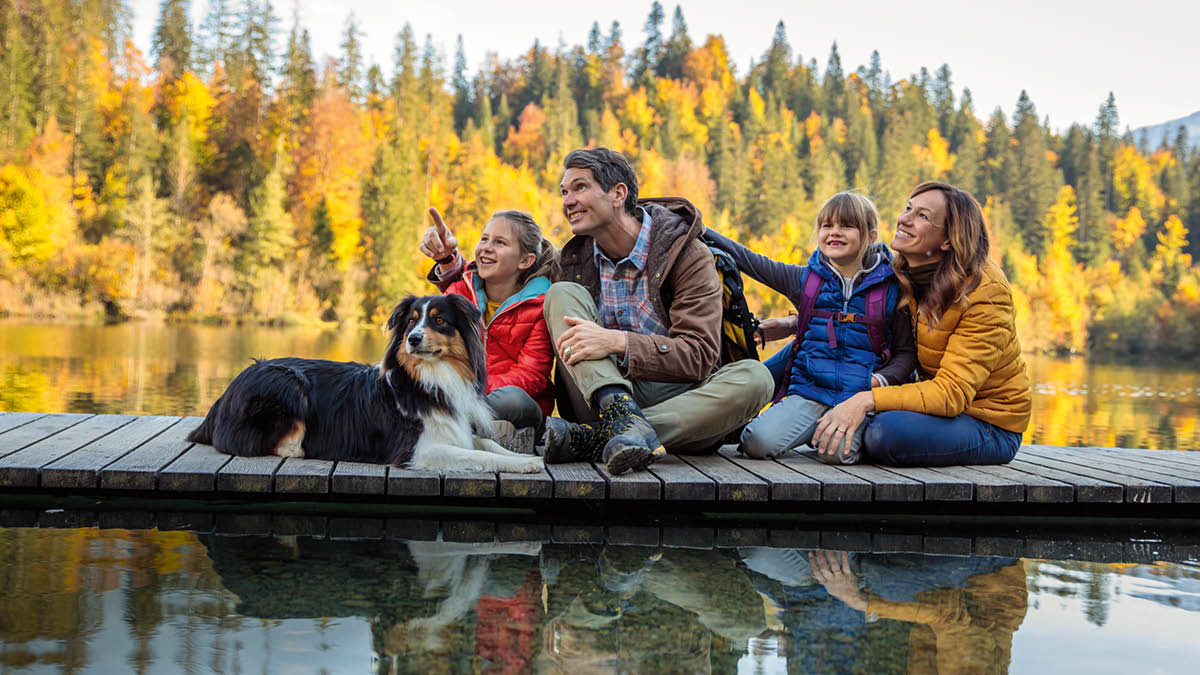 Ein Elternpaar mit zwei Kindern sitzt auf einem Steg; die Familie genießt gemeinsam die Natur.