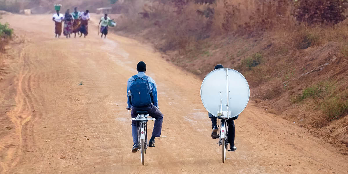 Zwei Brüder mit ihren Fahrrädern auf einer unbefestigten Straße. Sie bringen eine Satellitenanlage zu ihrem Königreichssaal.