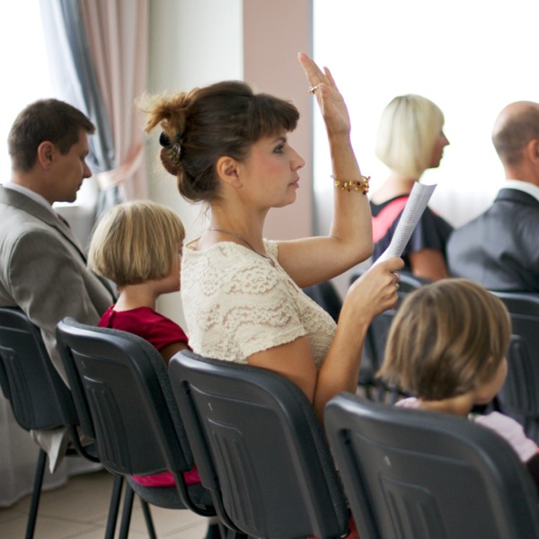 Eine Zeugin Jehovas meldet sich in einer Zusammenkunft durch Handzeichen