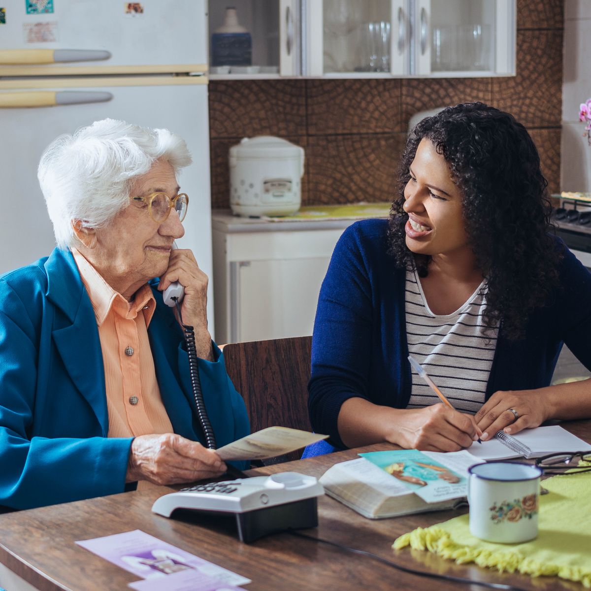 Eine Schwester unterstützt eine ältere Schwester beim Telefondienst und redet ihr aufmunternd zu.