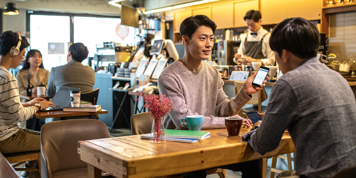 In einem Café zeigt ein Mann seinem Freund etwas auf seinem Smartphone.