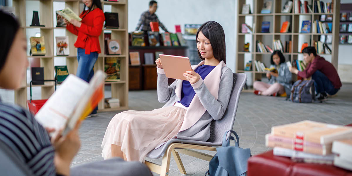 Eine Frau liest in der Bibliothek auf ihrem Tablet in der Bibel.