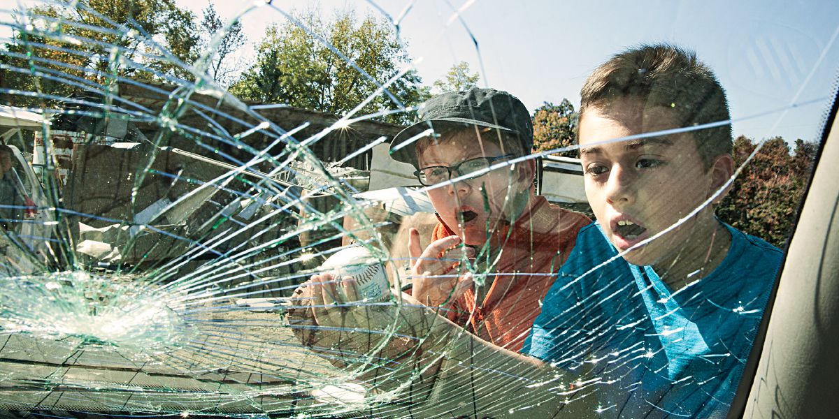 Zwei Jungen schauen erschrocken auf eine zersprungene Windschutzscheibe