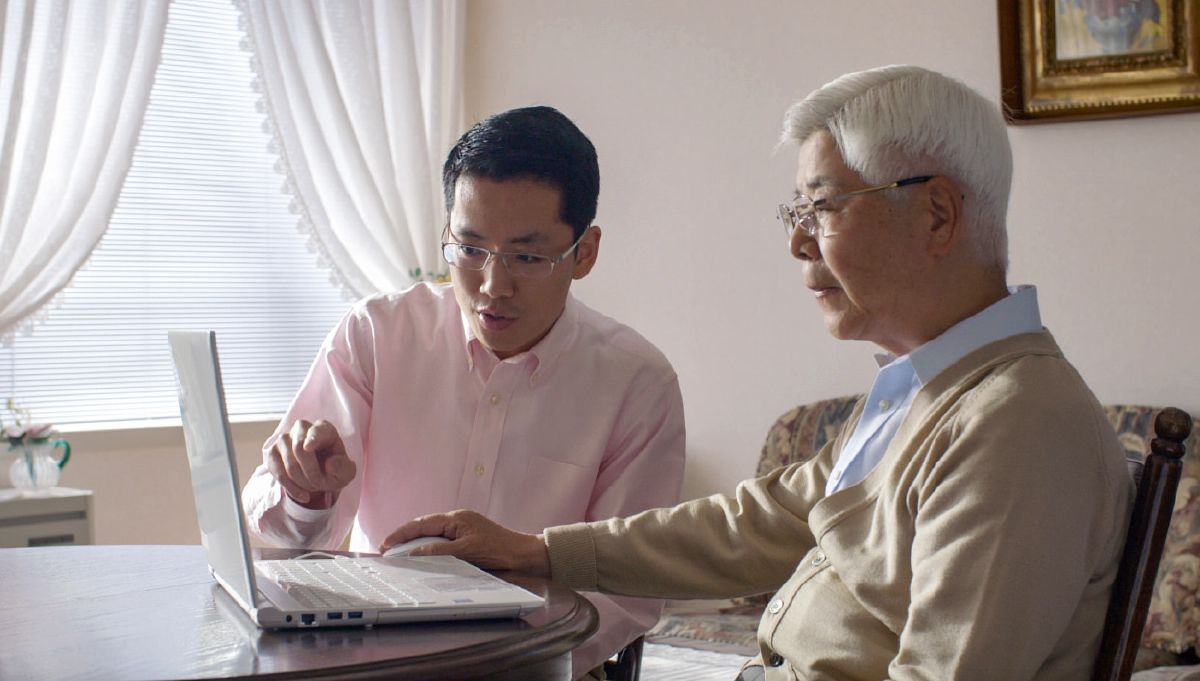 Un hermano joven ayudando a un hermano mayor a hacer donaciones usando un dispositivo electrónico