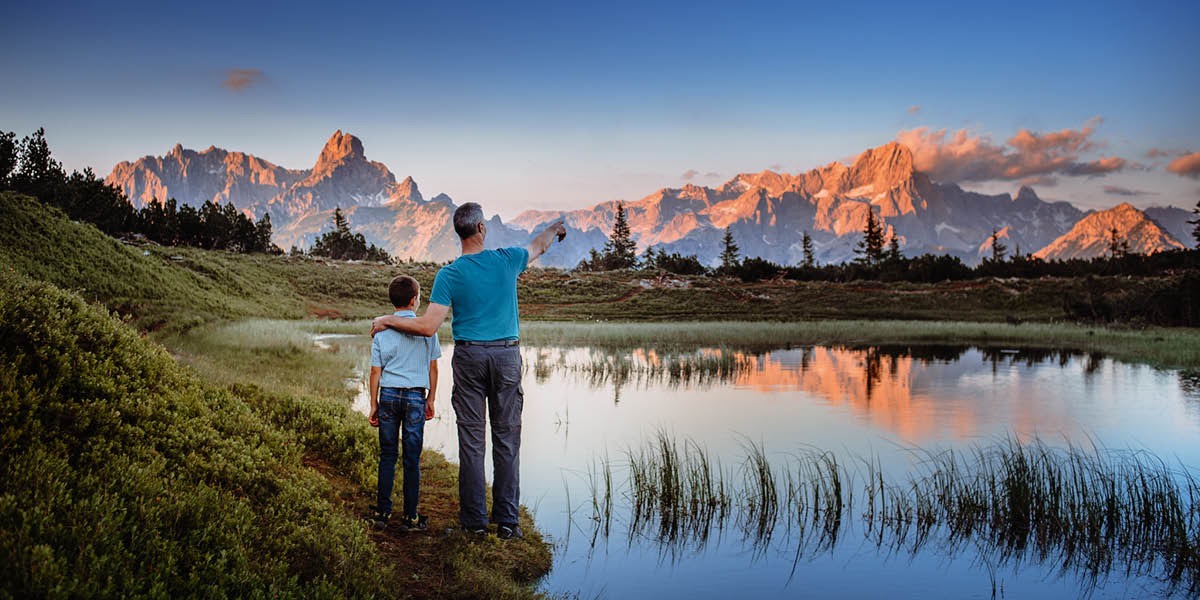 Un padre y su hijo de pie junto a un lago mirando las montañas