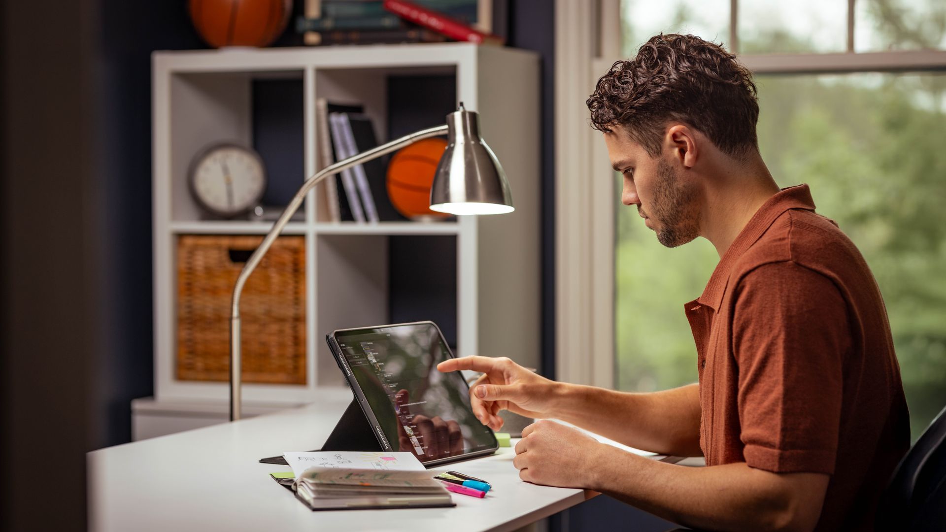 Un hermano joven está haciendo su estudio personal con la Biblia, una tableta y un cuaderno, y está anotando algo en la Biblia.