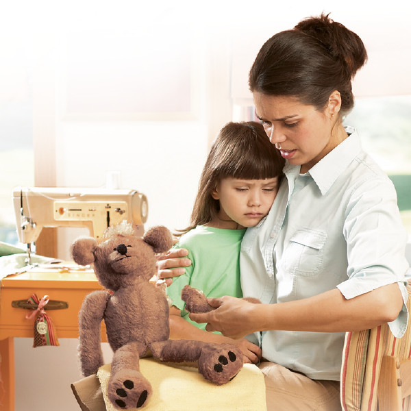 A mother consoling her daughter who is upset because an arm has come off her teddy bear.