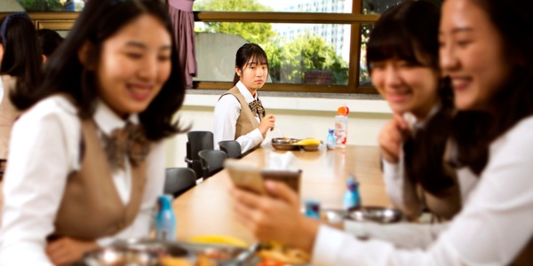 A girl sits alone and watches other girls talk and laugh together