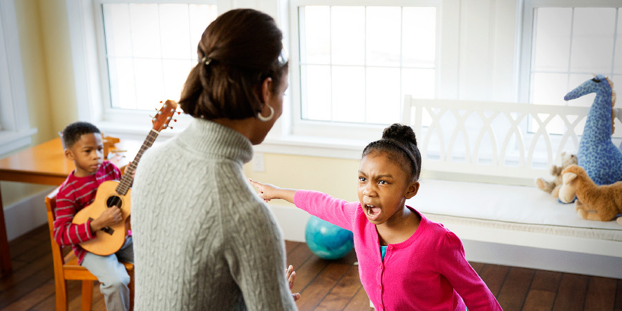 A little girl angrily shouts at her mother and points at her brother