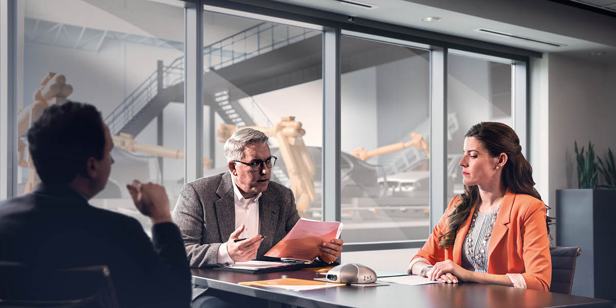 Two men interviewing a woman for a job at an automobile factory. She appears tense.