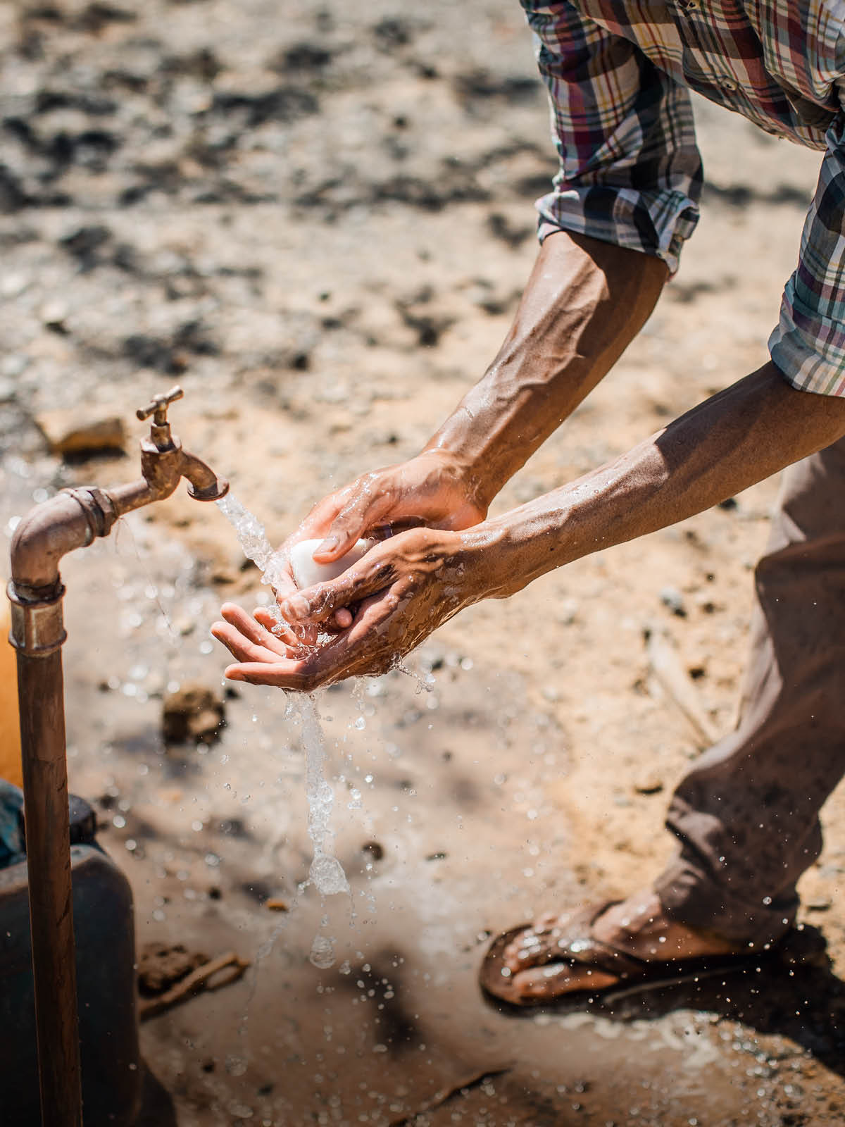 A man washing his hands with soap and water outdoors.