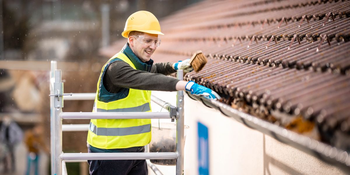 A brother on a scaffold, cleaning leaves from a gutter at a Kingdom Hall.