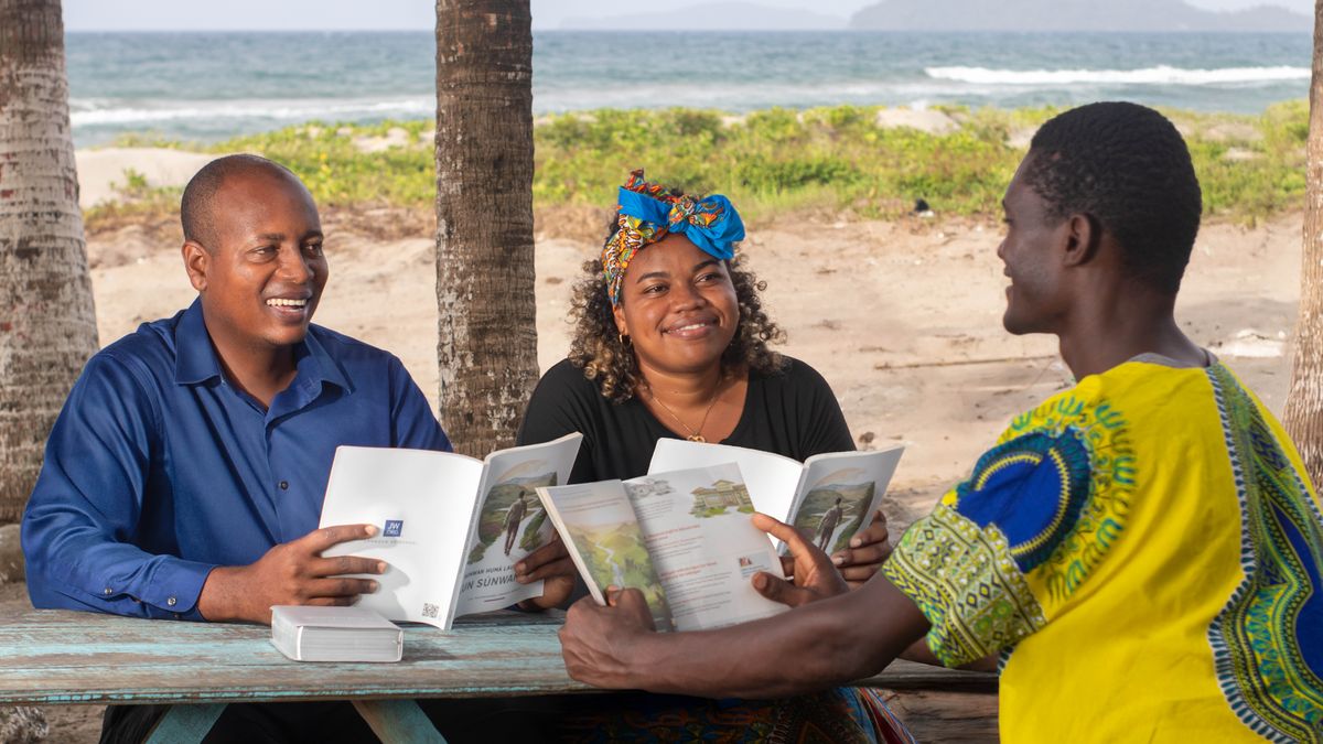 A couple using the “Enjoy Life Forever!” book to study with a man outdoors near the beach.