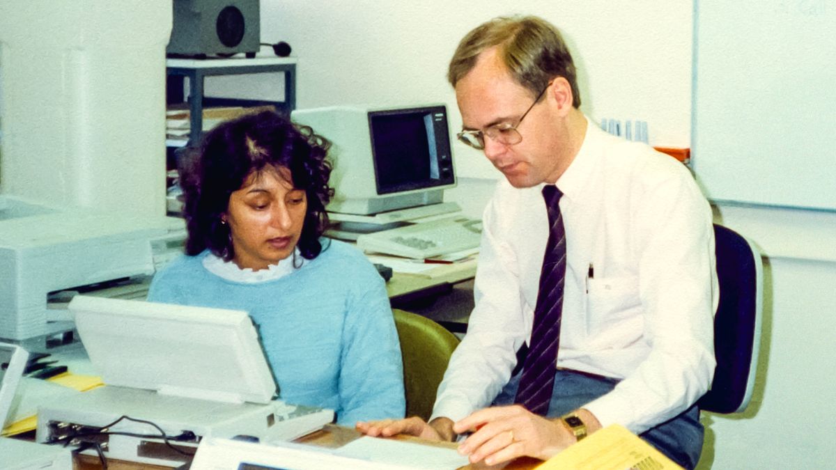 Kamal sitting at a computer terminal and receiving training from a brother.