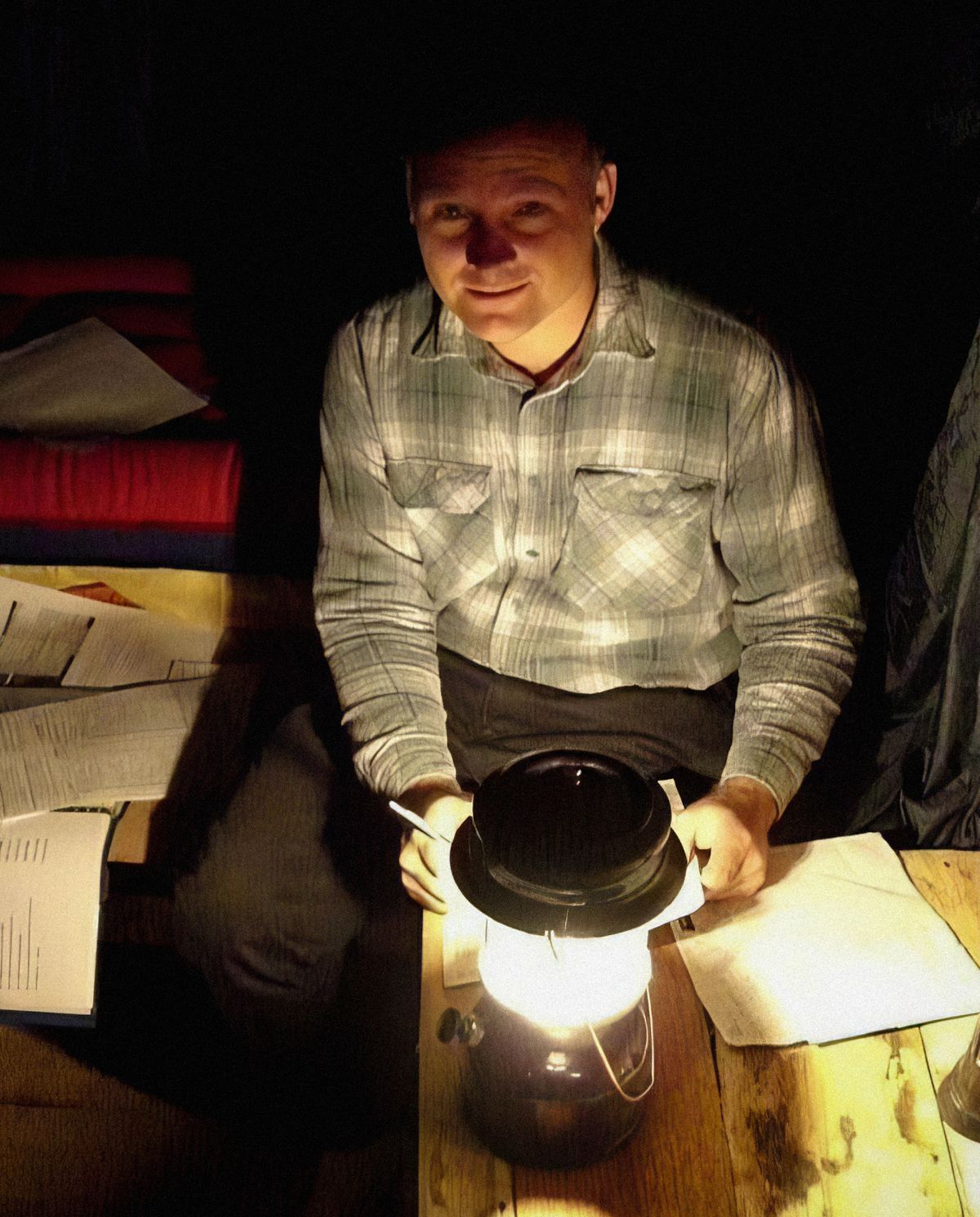 Warren using a lantern at night as he prepares reports.