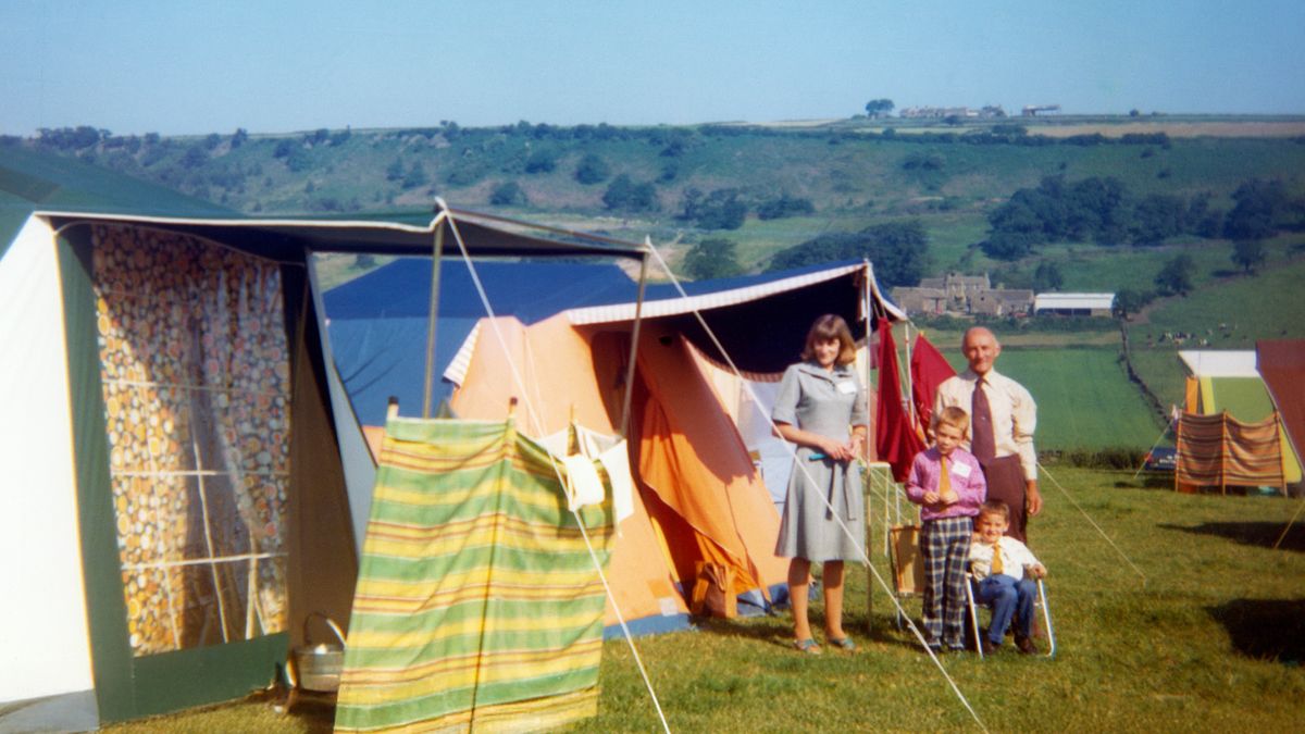 Carol with her father and two of her sons, standing near their camping tents.