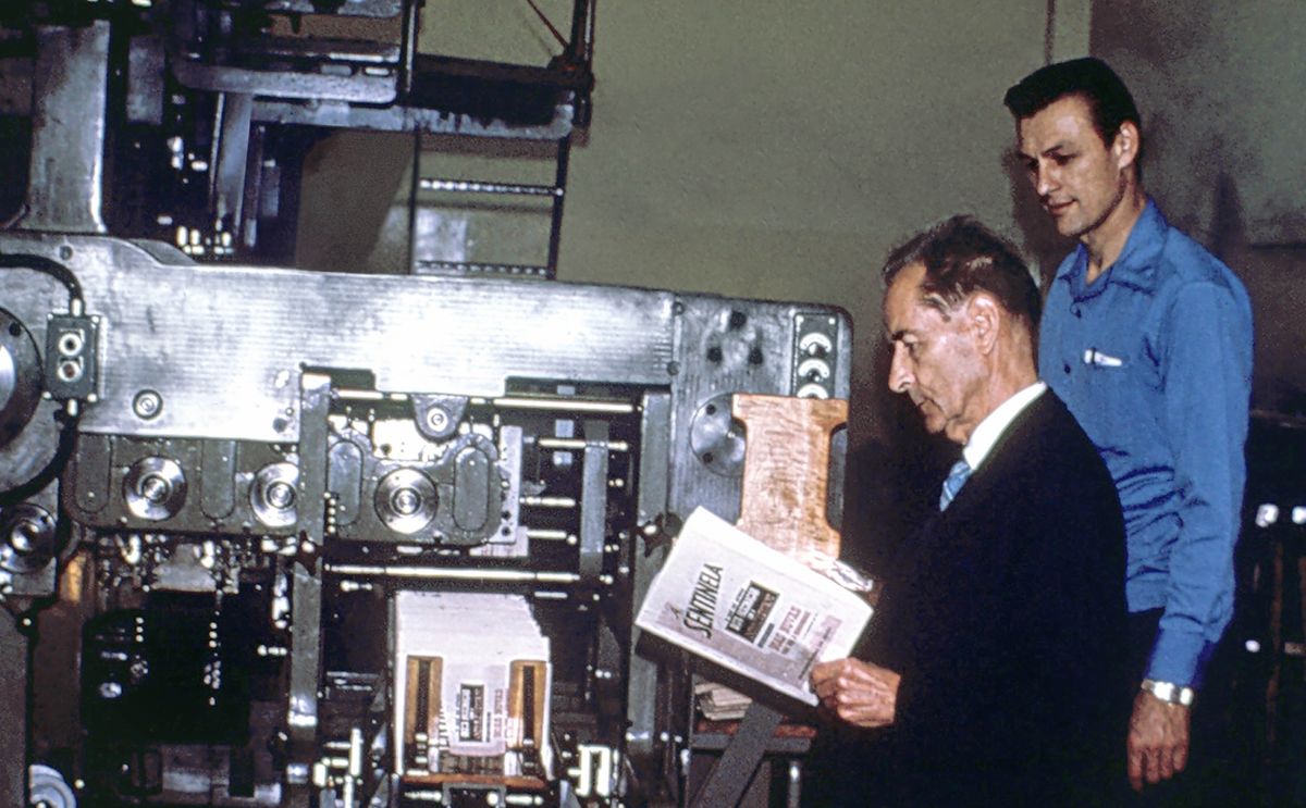 Karl standing beside Brother Franz as he examines a Portuguese copy of “The Watchtower” that has just come off a large printing press.