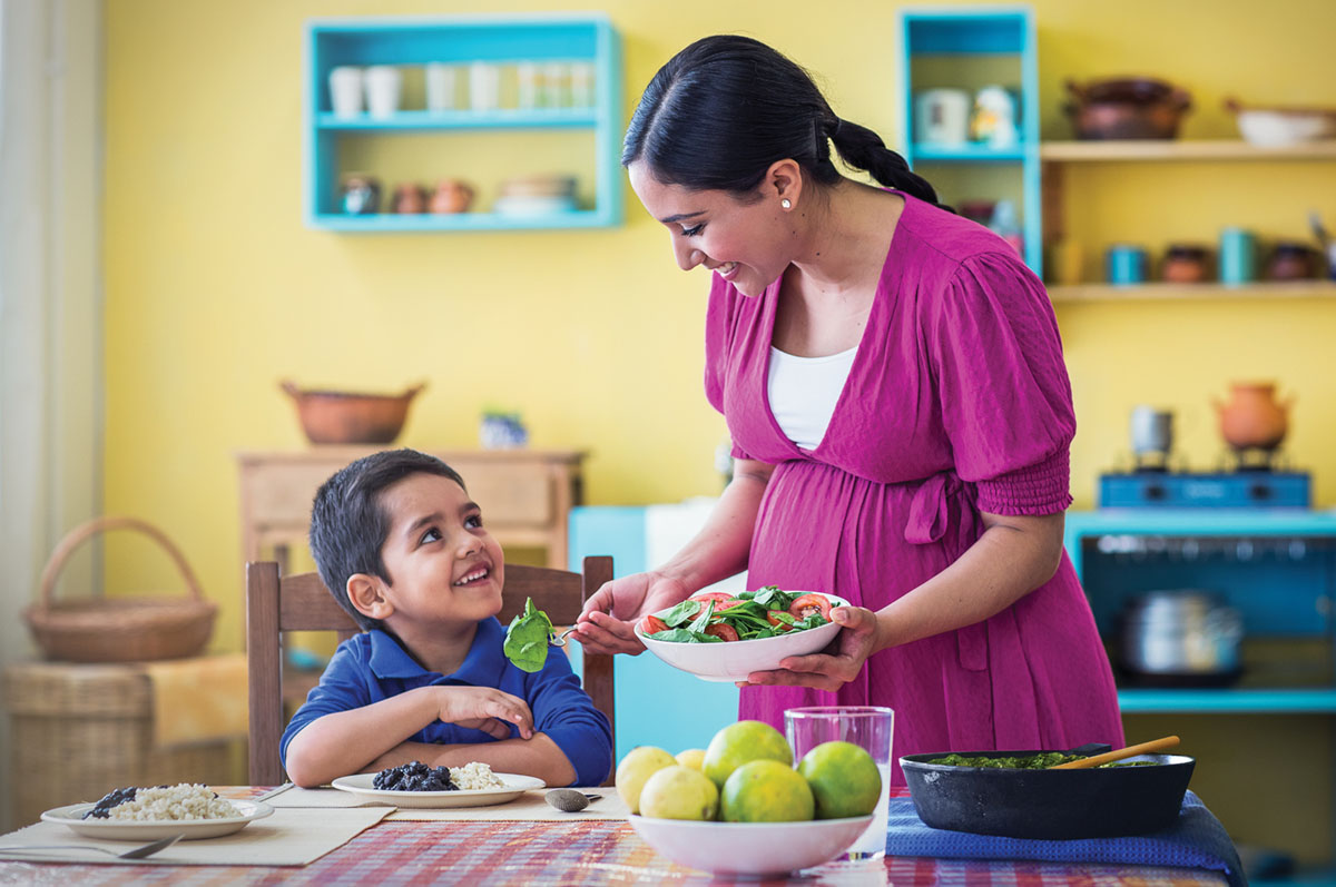 A pregnant woman serves her little boy and herself a healthy meal