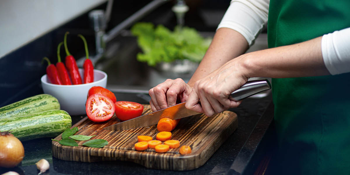 A woman chopping fresh vegetables on a wooden cutting board.