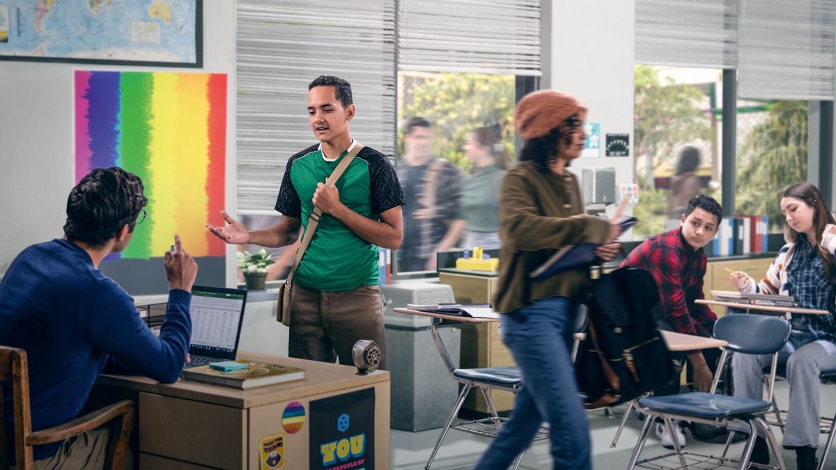 A teenage Witness respectfully explaining his beliefs to a teacher in a classroom. The classroom is decorated with rainbow flags to support gay rights.