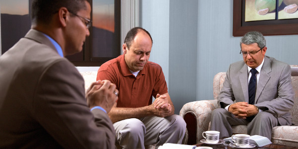 Congregation elders praying with an inactive Christian brother