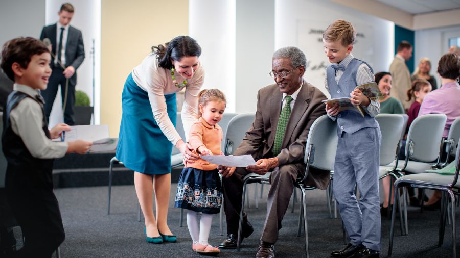 An elder chatting with young children at the Kingdom Hall and looking at pictures they have drawn.